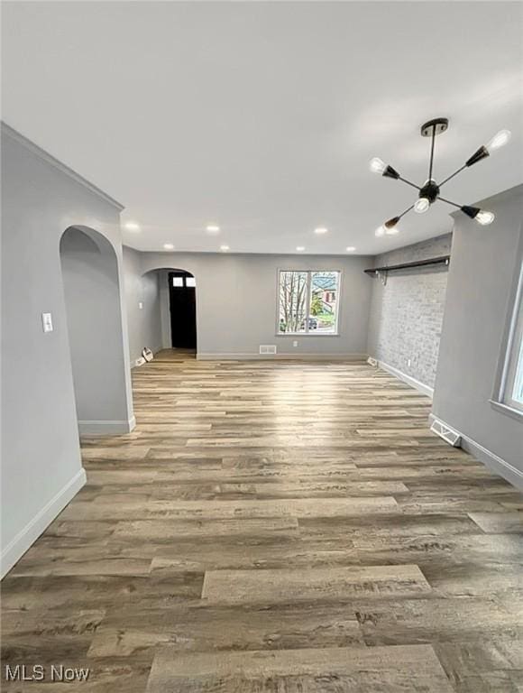 unfurnished living room featuring arched walkways, visible vents, baseboards, and wood finished floors