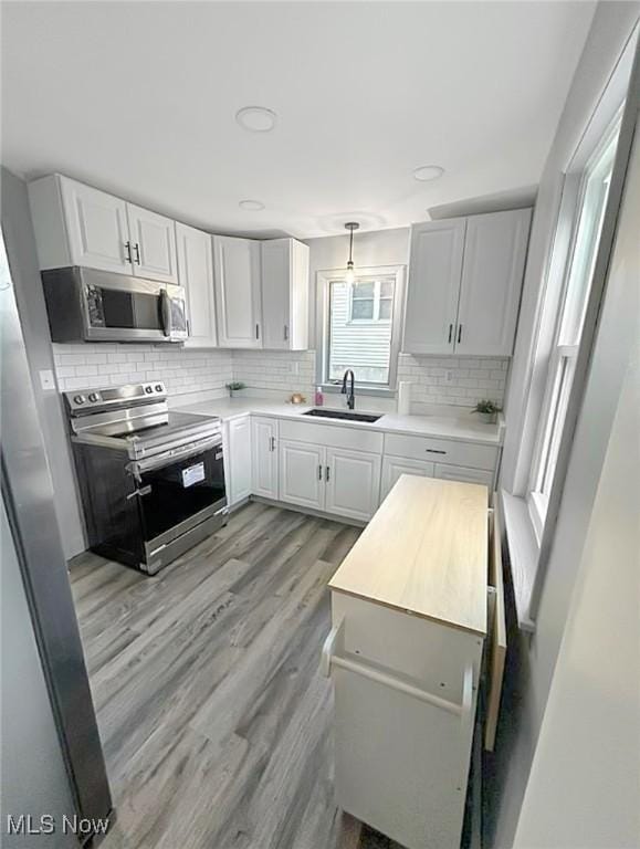 kitchen featuring light wood-style flooring, a sink, stainless steel appliances, light countertops, and backsplash