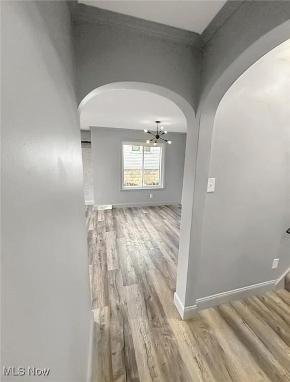 hallway featuring an inviting chandelier, baseboards, and wood finished floors