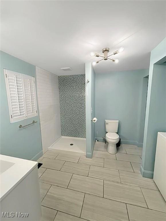 bathroom featuring baseboards, tiled shower, vanity, and toilet