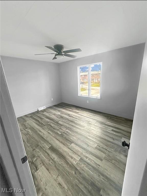 empty room featuring a ceiling fan, visible vents, and wood finished floors