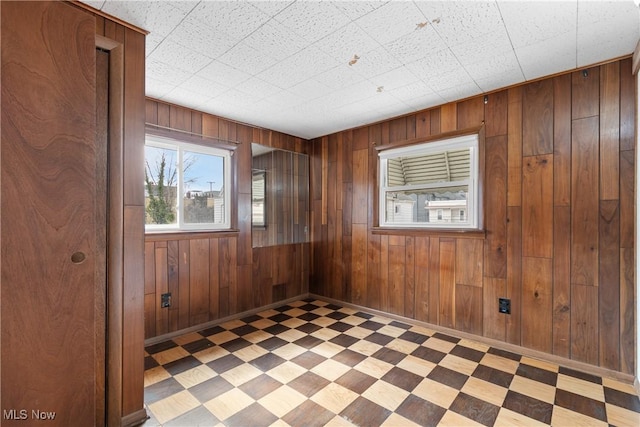 spare room featuring baseboards, wood walls, and tile patterned floors