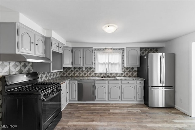 kitchen featuring a sink, stainless steel appliances, light wood-type flooring, under cabinet range hood, and backsplash