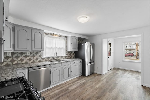 kitchen with light wood-style flooring, decorative backsplash, gray cabinetry, appliances with stainless steel finishes, and a sink