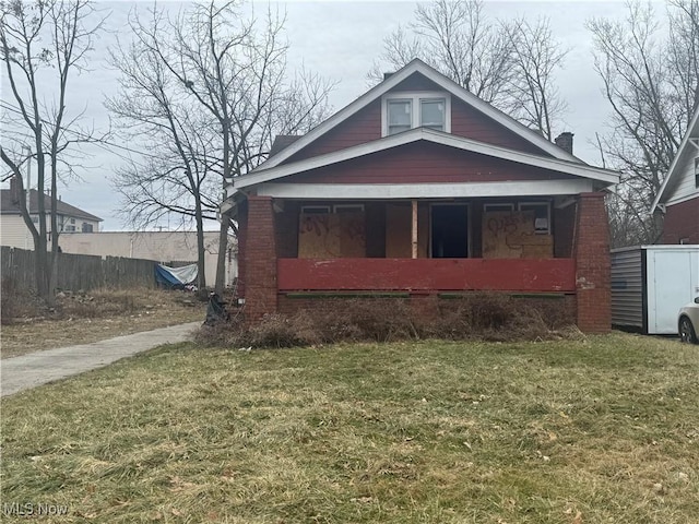 bungalow-style home with a porch, a front yard, fence, and brick siding