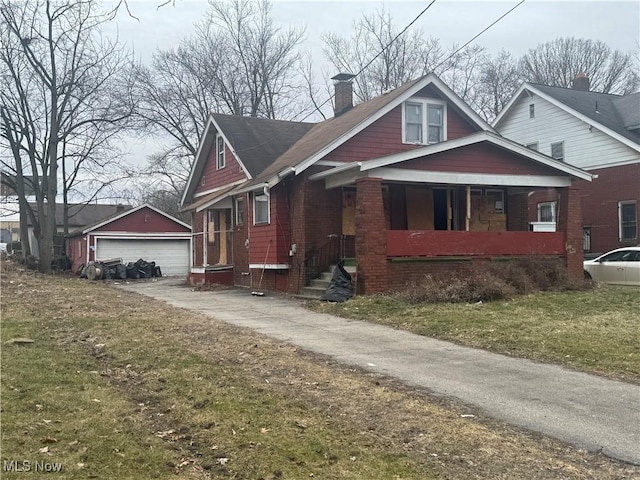 bungalow-style home featuring brick siding, a detached garage, a chimney, and an outdoor structure