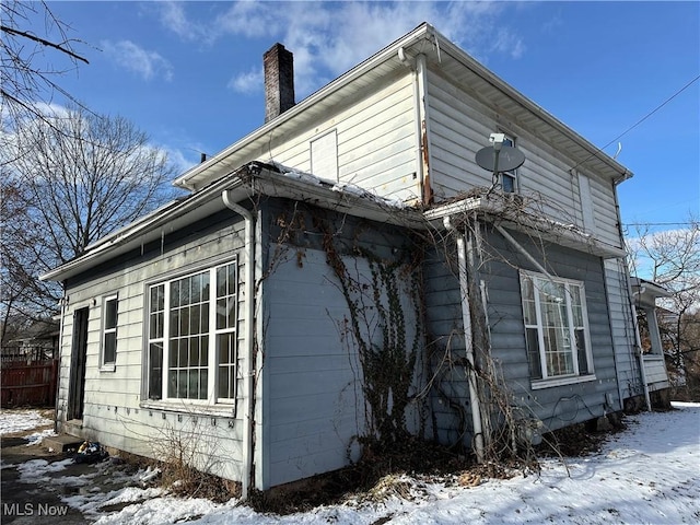 snow covered property featuring fence and a chimney