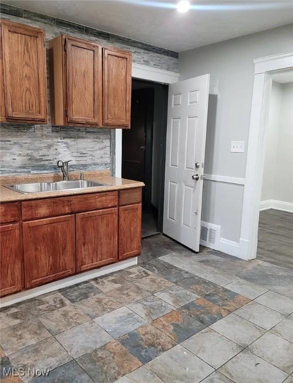 kitchen featuring a sink, visible vents, baseboards, light countertops, and tasteful backsplash