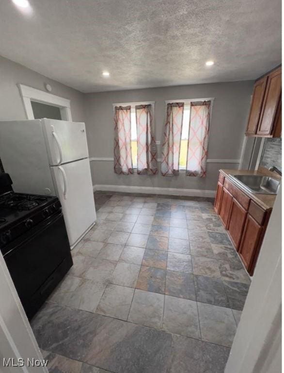 kitchen with a textured ceiling, a sink, baseboards, brown cabinetry, and gas stove