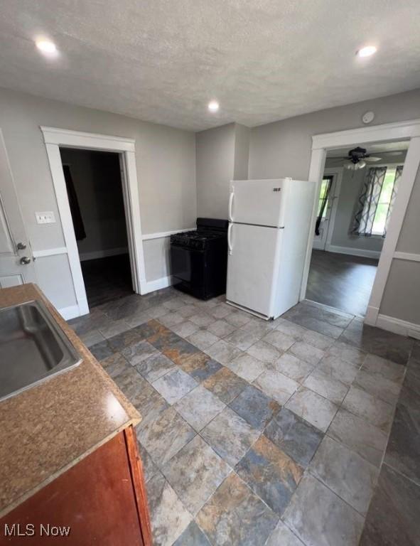 kitchen featuring baseboards, ceiling fan, freestanding refrigerator, a textured ceiling, and a sink