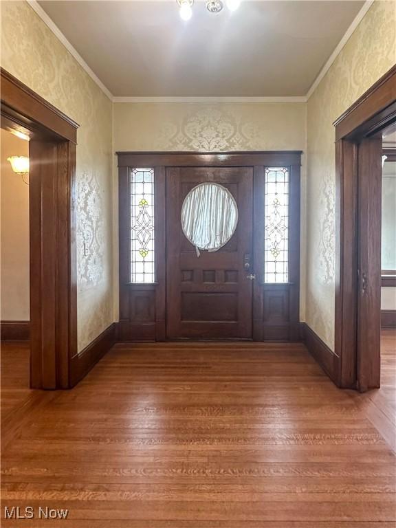 foyer with a textured wall, baseboards, crown molding, and wood finished floors