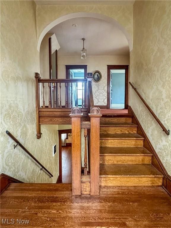 staircase with hardwood / wood-style flooring and arched walkways