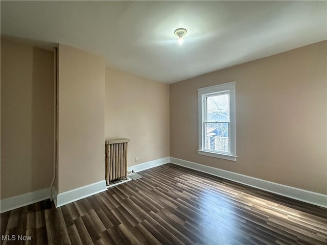 spare room with baseboards, dark wood-style flooring, and radiator