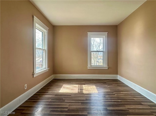 empty room featuring plenty of natural light, dark wood finished floors, and baseboards