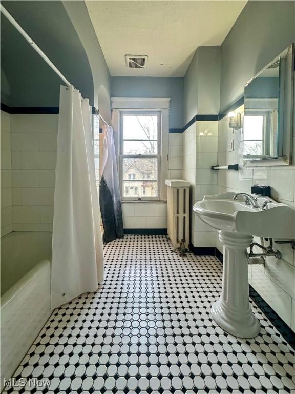 bathroom with visible vents, radiator heating unit, tile patterned floors, shower / bath combo with shower curtain, and tile walls