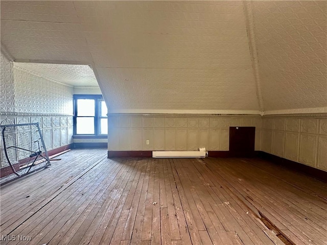 additional living space featuring a baseboard heating unit, lofted ceiling, and hardwood / wood-style flooring