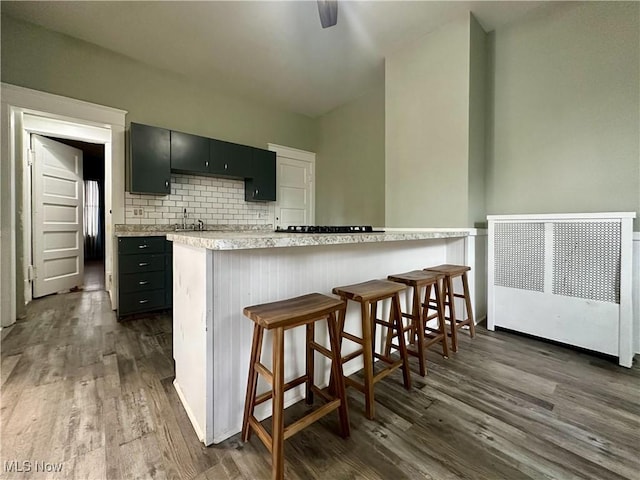 kitchen with tasteful backsplash, dark wood-style flooring, light countertops, dark cabinetry, and a kitchen bar