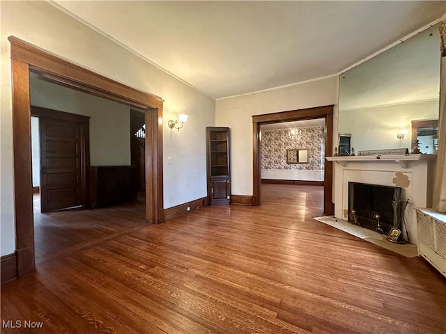 unfurnished living room with a fireplace with flush hearth, ornamental molding, wood finished floors, and baseboards