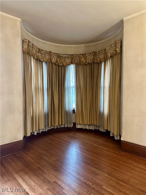 unfurnished room featuring baseboards, dark wood-style flooring, and crown molding