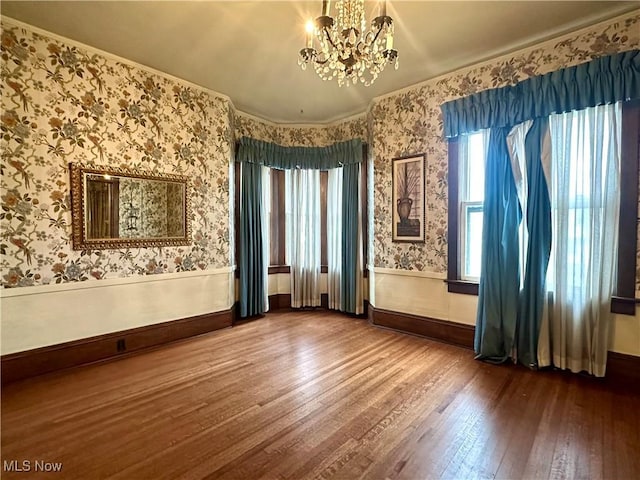 empty room featuring wood-type flooring, a notable chandelier, a wainscoted wall, plenty of natural light, and wallpapered walls