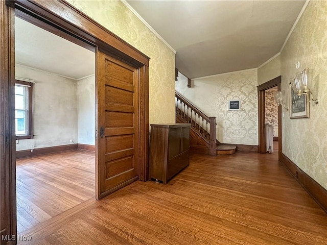 hall featuring wood finished floors, crown molding, stairway, and wallpapered walls