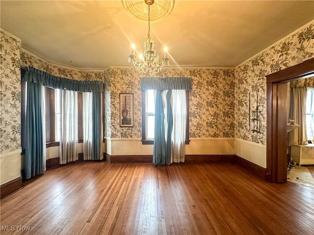 unfurnished room with a notable chandelier, hardwood / wood-style floors, wainscoting, and wallpapered walls