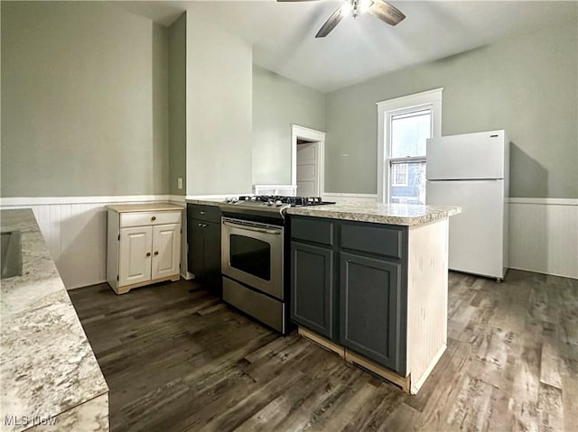 kitchen featuring wainscoting, gas range, dark wood-type flooring, freestanding refrigerator, and a peninsula