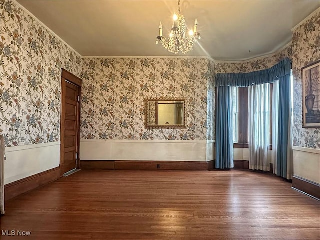 empty room with wallpapered walls, a chandelier, a wainscoted wall, and wood finished floors