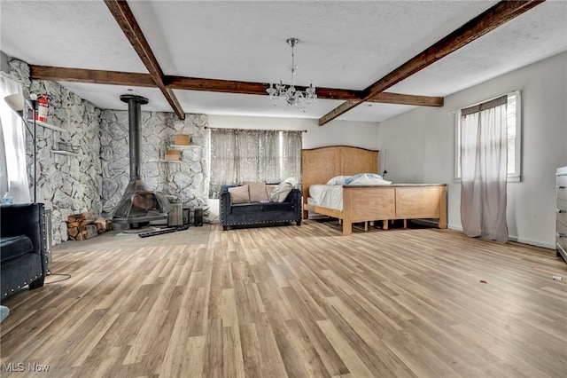 bedroom featuring a wood stove, a chandelier, wood finished floors, and beamed ceiling