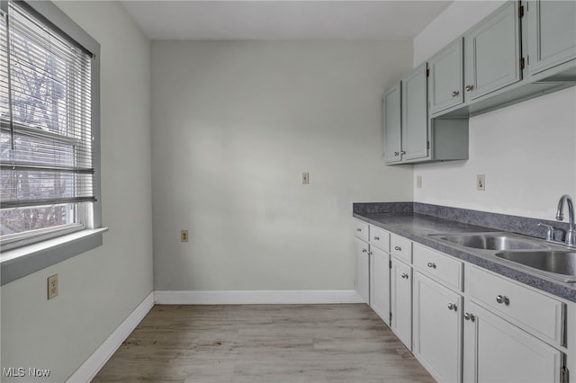 kitchen featuring dark countertops, baseboards, a sink, and light wood finished floors