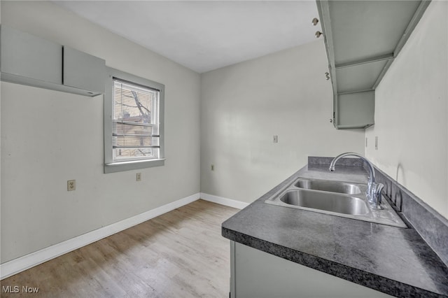 kitchen with light wood-style floors, dark countertops, a sink, and baseboards