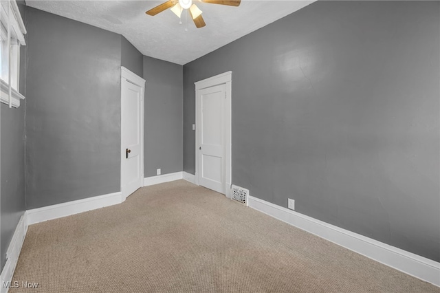 spare room with baseboards, visible vents, a ceiling fan, carpet, and a textured ceiling