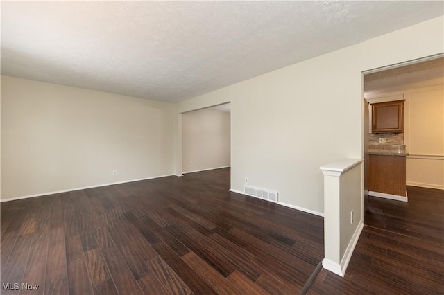 unfurnished room with dark wood-style floors, visible vents, and baseboards