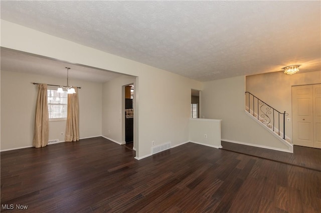 unfurnished living room featuring visible vents, dark wood-style flooring, stairs, a textured ceiling, and a notable chandelier