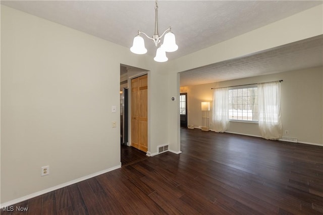 unfurnished room with dark wood-style flooring, visible vents, a textured ceiling, a chandelier, and baseboards