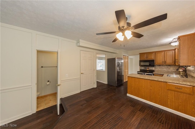 kitchen with stainless steel appliances, a peninsula, dark wood-style flooring, a sink, and brown cabinetry