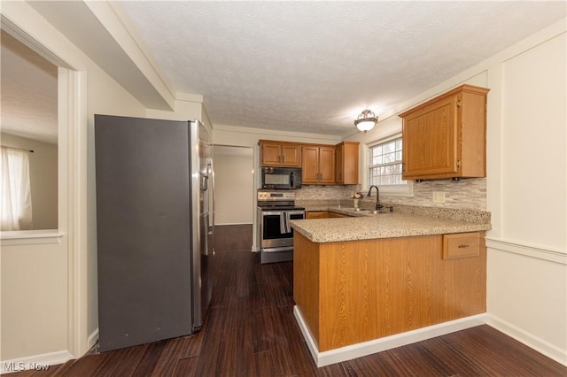 kitchen with stainless steel appliances, a peninsula, a sink, light countertops, and dark wood-style floors