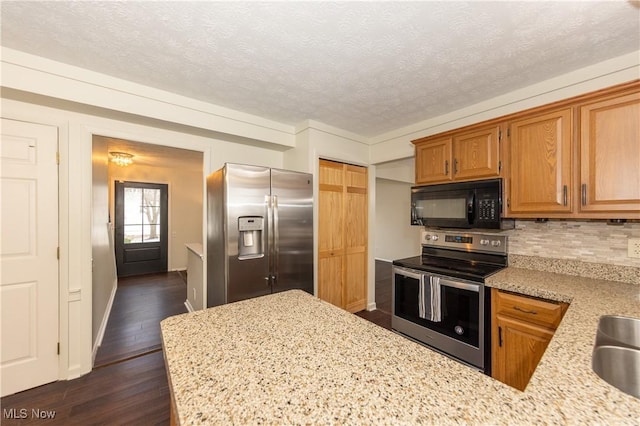 kitchen with a textured ceiling, light stone countertops, stainless steel appliances, decorative backsplash, and dark wood-style floors