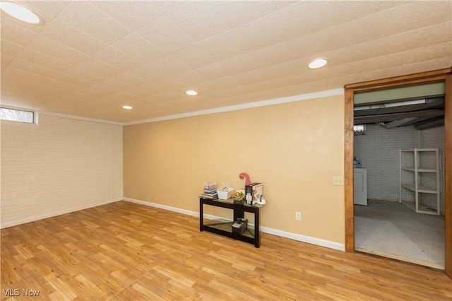 finished basement featuring baseboards, brick wall, light wood-style flooring, washer / clothes dryer, and ornamental molding