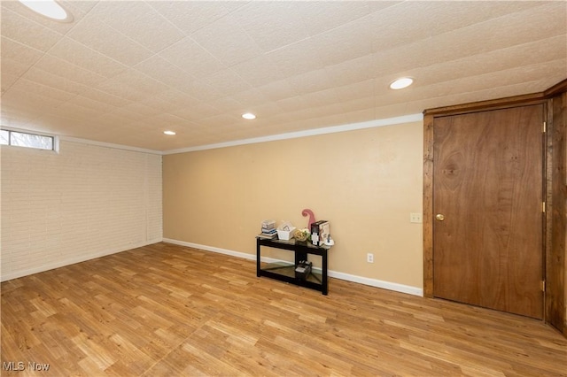 below grade area featuring light wood-type flooring, baseboards, crown molding, and brick wall