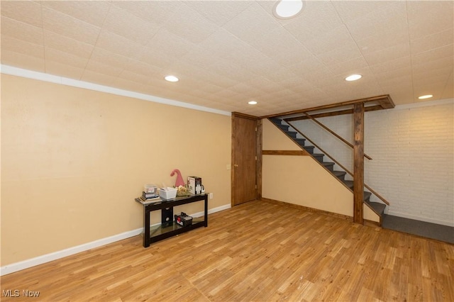 finished below grade area featuring recessed lighting, brick wall, wood finished floors, baseboards, and stairway