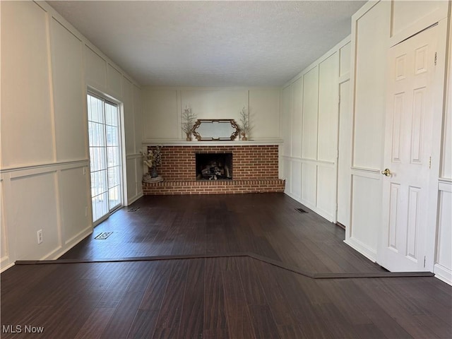 unfurnished living room featuring a fireplace, visible vents, a decorative wall, and dark wood-type flooring