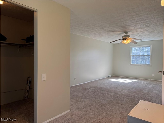 empty room featuring carpet floors, a ceiling fan, baseboards, and a textured ceiling