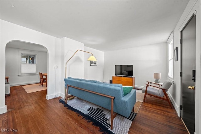 living room featuring baseboards, arched walkways, and dark wood-type flooring