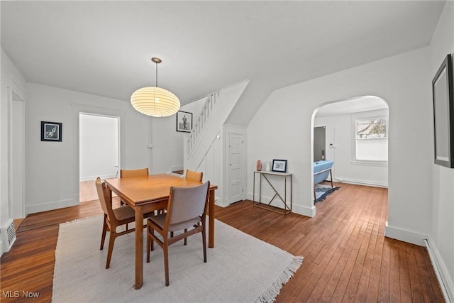 dining space featuring arched walkways, baseboards, stairway, and hardwood / wood-style floors