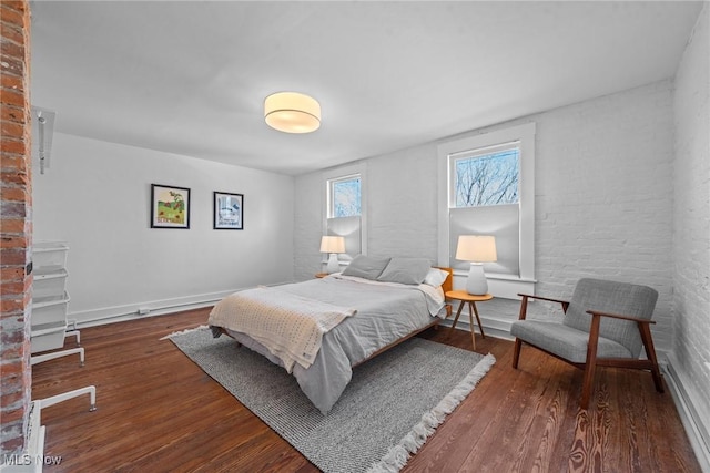 bedroom featuring brick wall and wood finished floors