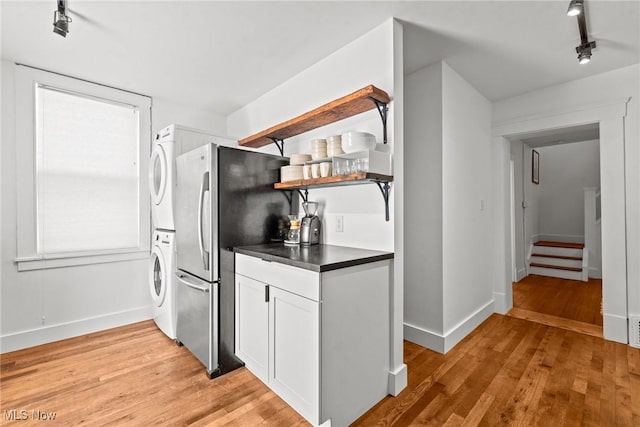 kitchen with light wood-style floors, stacked washer / dryer, dark countertops, and open shelves