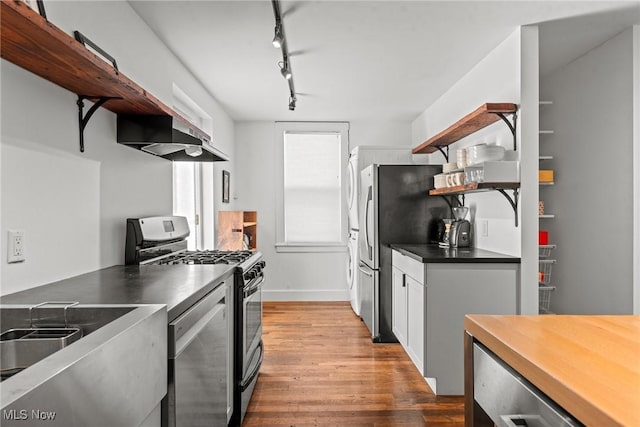 kitchen with wood finished floors, exhaust hood, appliances with stainless steel finishes, open shelves, and dark countertops