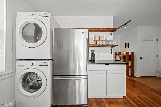 washroom with dark wood-style floors, track lighting, and stacked washer / dryer