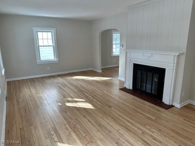 unfurnished living room with a large fireplace, light wood-style flooring, arched walkways, and baseboards